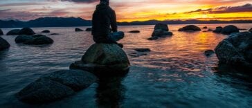 person sitting on rock on body of water
