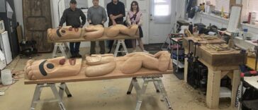 People assemble around carved wooden sculptures on tables